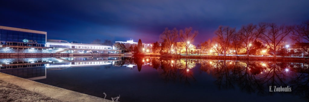 Nachtaufnahme am Unteren See in Böblingen. Im See spiegeln sich die hellen Lichter der Kongresshalle und rechts die Bäume mit der nächtlichen Beleuchtung am Weg