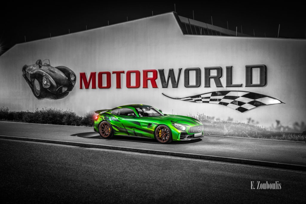 Schwarzweiss-Aufnahme eines Sievers Performance AMG GTR Green Tiger in grün. Im Hintergrund ist das Gebäude der Motorworld mit roter Aufschrift am Flugfeld Böblingen zu sehen