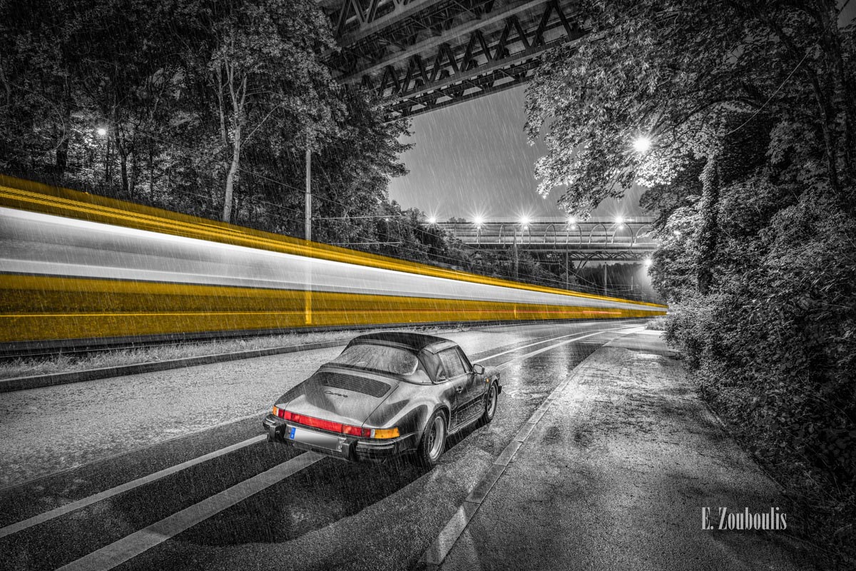 Ein Porsche Carrera 911 nachts auf nasser Straße im Regen mit einer vorbeiziehenden Straßenbahn Ein Porsche Carrera 911 nachts auf nasser Straße im Regen mit einer vorbeiziehenden Straßenbahn