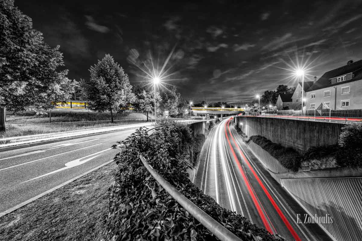 Der Verkehr nachts in Stuttgart Feuerbach. Autos mit roten und weißen Lichtern erhellen die Straße während eine gelbe Straßenbahn im Hintergrund die Brücke passiert