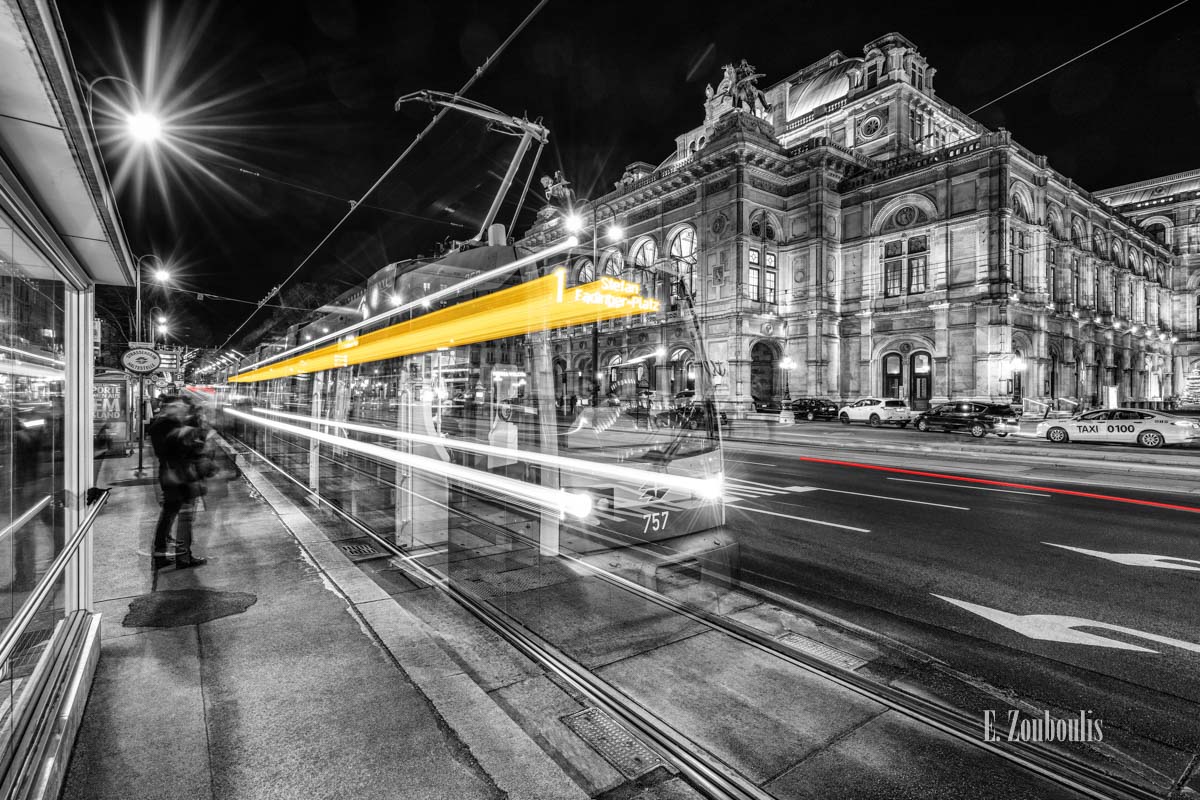 Bild einer Tram vor der Oper in Wien am Opernring. Schwarzweiß mit gelben und roten Light Trails