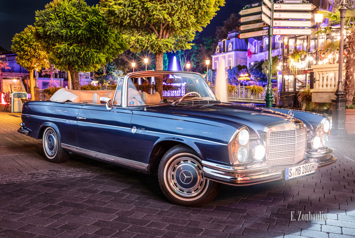 Ein 1971 Mercedes-Benz 280 SE nachts im Europa-Park seitlich von vorne mit den Lichtern des Europapark im Hintergrund Ein 1971 Mercedes-Benz 280 SE nachts im Europa-Park seitlich von vorne mit den Lichtern des Europapark im Hintergrund
